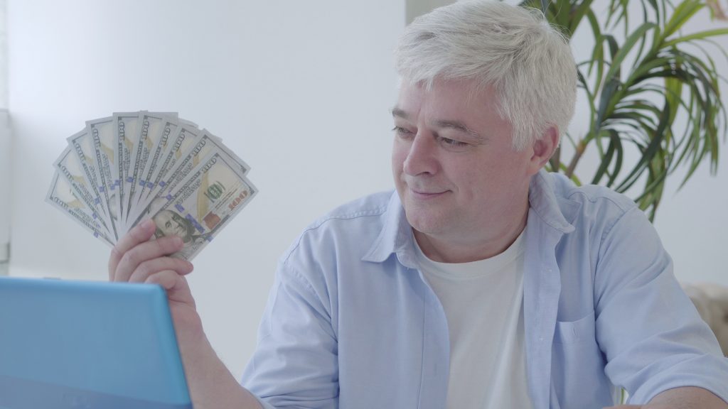 camera-approaches-to-happy-senior-man-bragging-pack-of-money-and-smiling-close-up-of-s-SBI-351310022