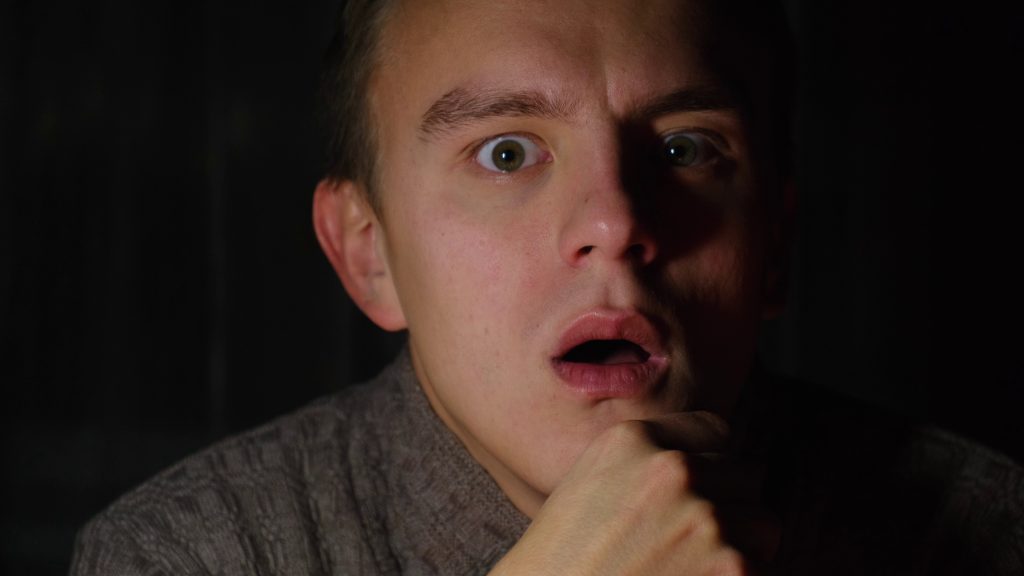 frightened-and-stunned-man-watching-a-movie-in-the-dark-SBI-350072378